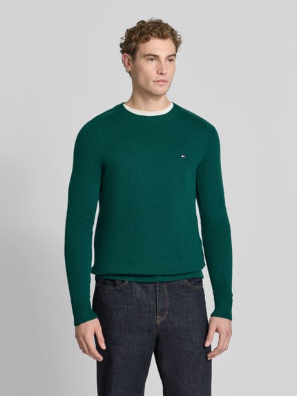 Męski model nosi Regular Fit Pullover aus Lammwoll-Mix von Tommy Hilfiger, zielony, imitacja dzianiny, faktura, detal z logo, długi rękaw, okrągły dekolt, prążkowane zakończenia, wykończenie: dzianina, drobny splot, Ganzkörperansicht von vorne.