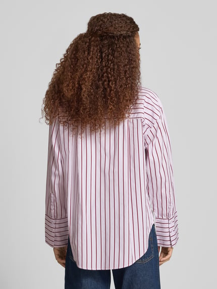 Männermodel trägt Oversized Hemdbluse mit Brusttasche von Gina Tricot, białe i bordowe paski, bawełna, krój oversized fit, Kołnierzyk typu kent, listwa guzikowa, brustasza, sportowe mankiety, zaokrąglony dół, długość tyłu w rozmiarze S: 71 cm, długość rękawa: 54 cm, Ganzkörperansicht Rückansicht.