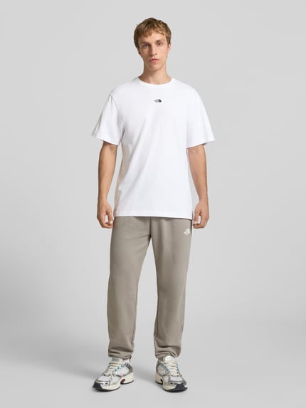 Männermodel trägt T-Shirt mit Logo-Stitching von The North Face aus reiner Baumwolle in Weiß, gerader Schnitt, Ganzkörperansicht von vorne.