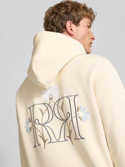 Männermodel trägt Relaxed Fit Hoodie mit Känguru-Tasche von REVIEW in Creme mit floraler Stickerei, Nahaufnahme Rückansicht. Baumwoll-Mix, elastische Abschlüsse.