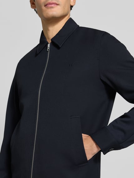 Männermodel trägt gerade, dunkelblaue Jacke mit Logo-Stitching Modell 'Como' von Les Deux, aus Material-Mix, Nahaufnahme Oberkörper.