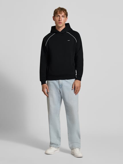 Männermodel trägt Hoodie mit Logoprint und Kontrastspipings von REVIEW aus Baumwoll-Mix in Schwarz, Regular Fit, Ganzkörperansicht von vorne.
