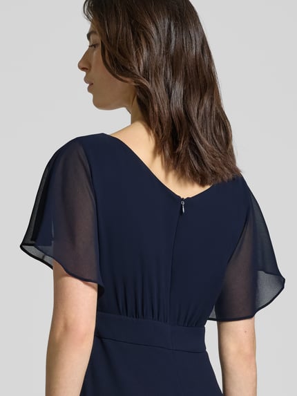 Vrouwenmodel draagt 'Knielanges Kleid mit Rundhalsausschnitt' van Vera Mont in semi-transparant, getailleerd design, korte mouwen, zichtdichte onderjurk, naadrits, donkerblauw, detailopname rugaanzicht.