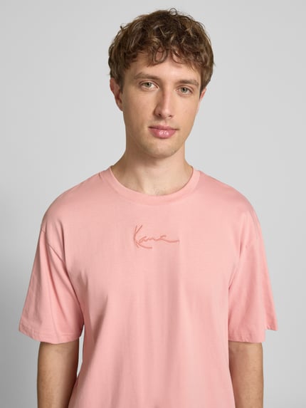 Männermodel trägt Regular Fit T-Shirt mit Logo-Stitching von KARL KANI in Rosa aus Reine Baumwolle, Rundhalsausschnitt, Nahaufnahme Oberkörper, Rückenlänge bei Größe M: 73 cm.