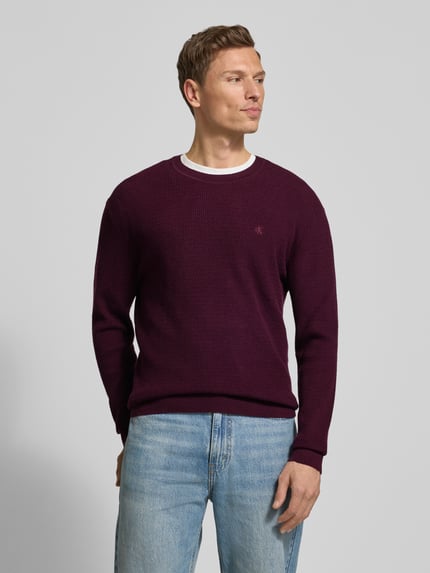 Männermodel trägt Strickpullover mit gerippten Abschlüssen von CK Calvin Klein in Dunkelrot, Baumwoll-Mix mit Stretch-Anteil, Regular-Fit, Label-Stitching, Rundhalsausschnitt, Ganzkörperansicht von vorne.