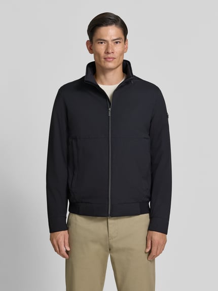 Männermodel trägt Regular Fit Jacke in Stepp-Optik von bugatti, schwarze Farbe, glatte Struktur, Stehkragen, Ganzkörperansicht von vorne.
