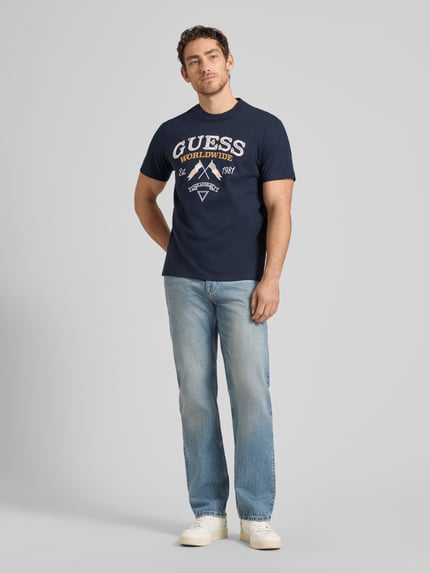 Männermodel trägt T-Shirt mit Rundhalsausschnitt und Label-Stitching von Guess in Dunkelblau, Baumwolle, Regular Fit, Ganzkörperansicht von vorne.