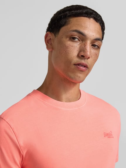 Männermodel trägt T-Shirt mit Rundhalsausschnitt und Label-Stitching von Superdry, Reine Baumwolle, Slim-Fit, Nahaufnahme Oberkörper.
