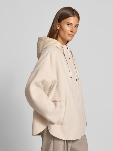 Frauenmodel trägt Jacke mit Kapuze von COMMA in Beige mit lockerer Passform, seitlichen Eingrifftaschen und Knopfleiste, Ganzkörperansicht von vorne.