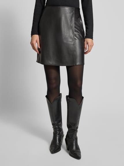Frauenmodel trägt Minirock in Leder-Optik Modell 'Reana cosmic' von OPUS, gerader Schnitt, Wickel-Optik, Eingrifftaschen, Farbe Schwarz, Ganzkörperansicht von vorne.