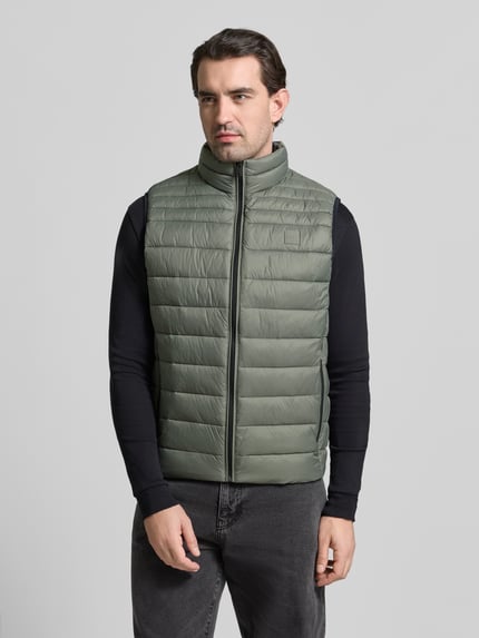 Männermodel trägt Regular Fit Steppweste mit Stehkragen Modell 'ODENO2' von BOSS Orange in Unifarben, Ganzkörperansicht von vorne.