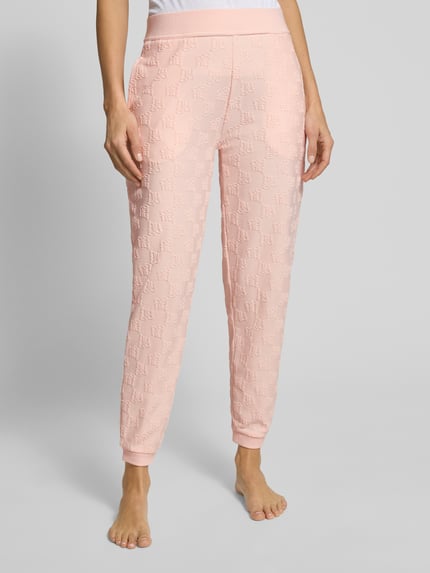 Frauenmodel trägt Slim Fit Sweatpants aus Baumwoll-Mix Modell 'TERRYMONOGRAM' von HUGO in Rosa mit Logo-Monogramm, Nahaufnahme Unterkörper.
