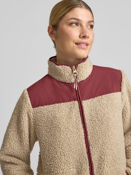 Vrouwenmodel draagt beige MOS MOSH fleecejack met opstaande kraag, Model 'Elisa Eli', tweewegritssluiting, steekzakken, regular fit, detailopname bovenlichaam. Ruglengte maat S: 58 cm, schouderbreedte: 41 cm, borstwijdte: 48 cm, mouwlengte: 63 cm.