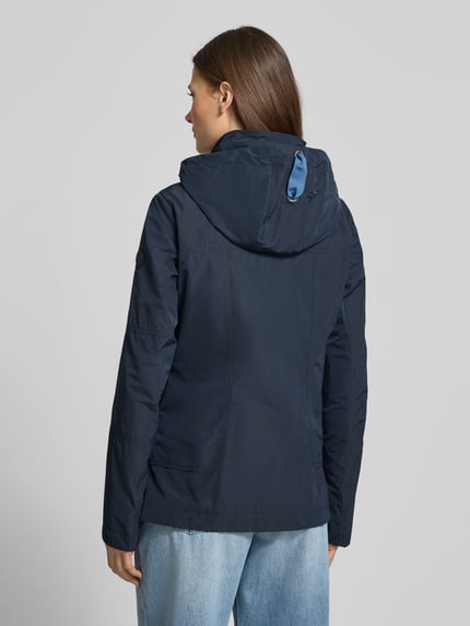 Modelka nosi Weather Protection Jack mit Reißverschlusstaschen od Gil Bret, krój regular fit, granatowy kolor, kaptur z troczkiem, stójka, zamek, listwa z guzikami, kieszenie na zamek, długość tyłu w rozmiarze 36: 66 cm, szerokość ramion w rozmiarze 36: 40 cm, szerokość w biuście w rozmiarze 36: 48 cm, długość rękawa w rozmiarze 36: 63 cm, widok całej sylwetki z tyłu