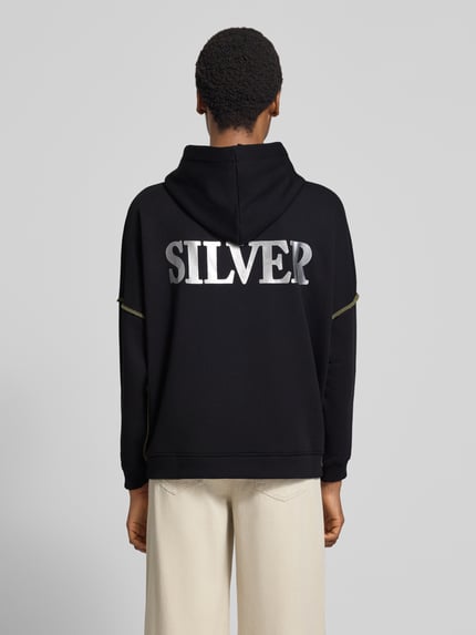 Frauenmodel trägt Oversized Hoodie aus reiner Baumwolle Modell 'Silver and Gold' von miss goodlife in Schwarz mit Statement-Print, Ganzkörperansicht Rückansicht.