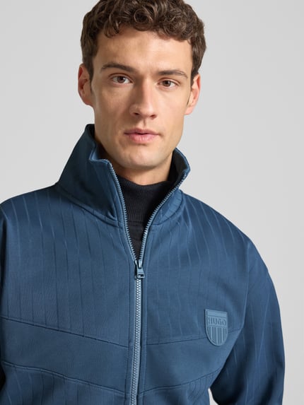 Męski model nosi Regular Fit Sweatjacke aus Baumwoll-Mix Modell 'DAVRONTO' od HUGO, granatowa, prążkowana, z zamkiem, zbliżenie na górę ciała.
