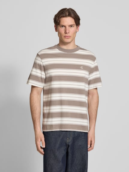 Männermodel trägt Regular Fit T-shirt aus katoenmix van Calvin Klein Jeans met gestreept all-over motief en gestikt logo, ronde hals, korte mouw, geheel in neutrale tinten, ganzkörperansicht van voren.