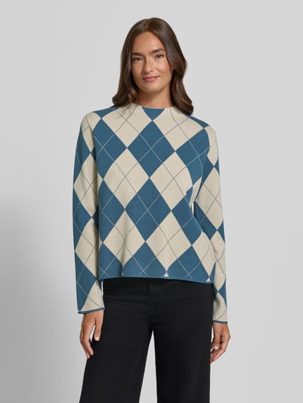 Modelka nosi sweter z dzianiny 'Strickpullover aus Viskose-Mix im Allover-Look' od COMMA, mieszanka wiskozy, krój regular fit, wzór na całej powierzchni, stójka, długość tyłu w rozmiarze 36 to 53 cm, długość rękawów w rozmiarze 36 to 58 cm, kolory niebieski i beżowy, wzór rombów, gładka faktura, widok na cały przód,