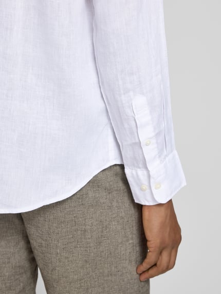 Männermodel trägt Regular Fit Freizeithemd aus reinem Leinen Modell 'REGKYLIAN' von SELECTED HOMME in Weiß, Nahaufnahme Unterkörper. Unifarbene Optik, Flammgarn-Struktur, Sportmanschette mit Knöpfen.
