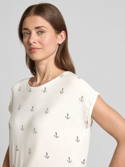 Modelka nosi Relaxed Fit T-Shirt aus Lyocell-Mix Modell 'AVA' od Vero Moda, jasny kolor, nadruk kotwicy, krótki rękaw, widok z przodu, zbliżenie na górną część ciała.
