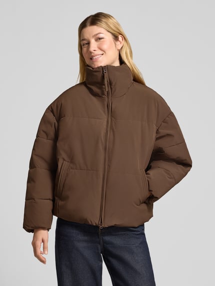 Frauenmodel trägt Steppjacke mit Stehkragen Modell 'Refron' von MSCH Copenhagen in Braun, Material-Mix mit Stretch, Ganzkörperansicht von vorne.