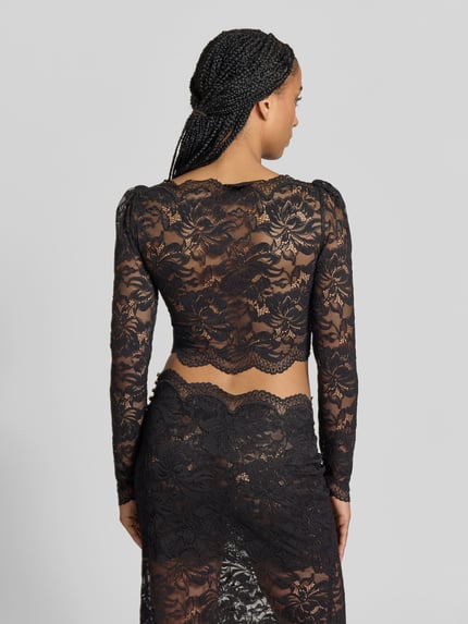 Frauenmodel trägt Cropped Langarmbluse aus Spitze von Rabanne in Schwarz, eng anliegend, semitransparent, elastischer Material-Mix, Rückenansicht Ganzkörperansicht.