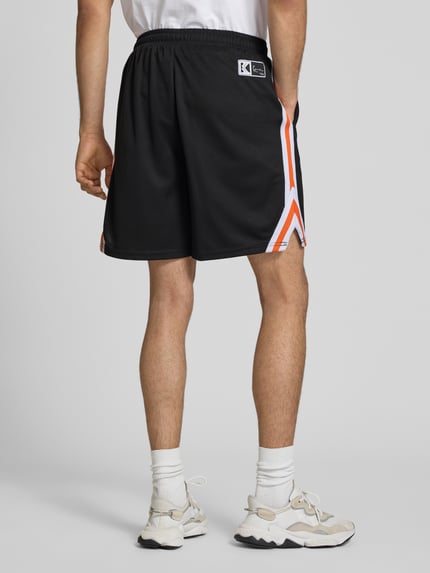 Männermodel trägt Regular Fit Shorts mit Logo-Print von KARL KANI in Schwarz mit Strukturmuster und elastischem Bund, Ganzkörperansicht Rückansicht.