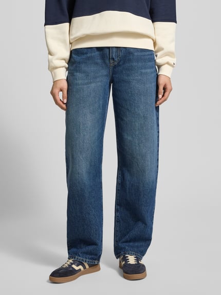 Männermodel trägt Tapered Fit Jeans aus reiner Baumwolle von Tommy Hilfiger in blauer Denim-Optik mit 5-Pocket-Design, Ganzkörperansicht von vorne.