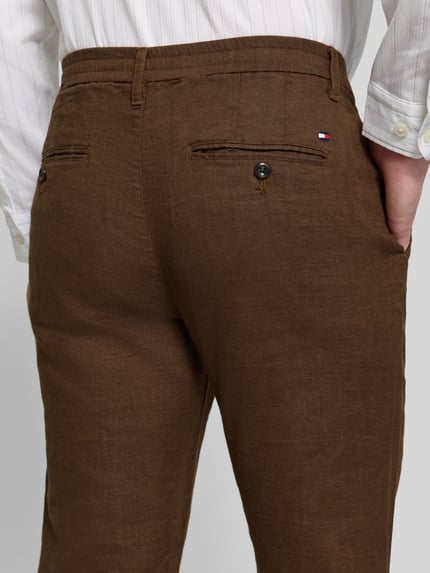 Mężczyznęmodel nosi Regular Fit Leinenhose mit Logo-Stitching Modell 'Denton' von Tommy Hilfiger, brązowy len, jednolity, detal logo, tylne kieszenie, zdjęcie z tyłu, zbliżenie na dolną część pleców.