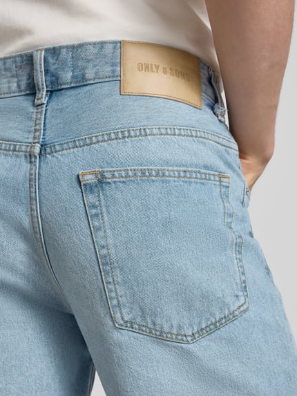 Männermodel trägt Straight Leg Jeansshorts aus reiner Baumwolle Modell 'EDGE' von Only & Sons, 5-Pocket-Design, Label Patch, Nahaufnahme Rückenansicht.