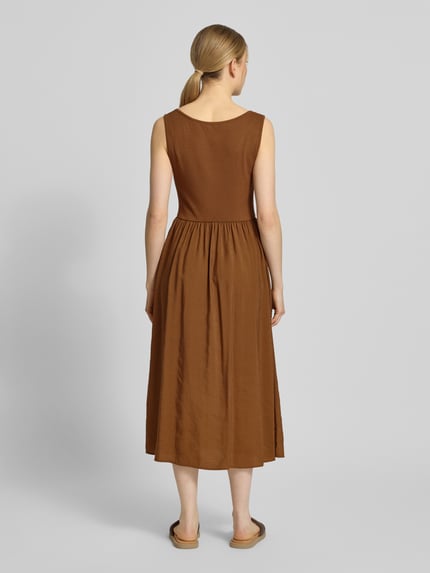 Modelka kobieca nosi Midikleid mit aufgesetzten Taschen od Rich & Royal, brązowa kolorystyka, krój slim fit, mikromodal, okrągły dekolt, brak rękawów, długość z tyłu 114 cm, szerokość w rozmiarze S: 32 cm, widok całej sylwetki od tyłu.