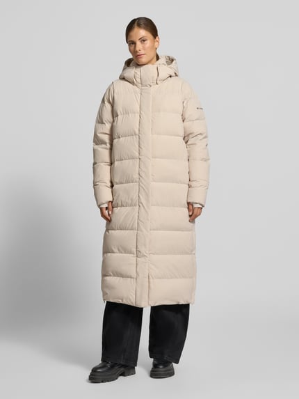 Modelka nosi Steppmantel mit Kapuze Modell 'Amaze' von Columbia, beżowy, materiał mix ze stretchem, krój regular fit, Ganzkörperansicht von vorne.