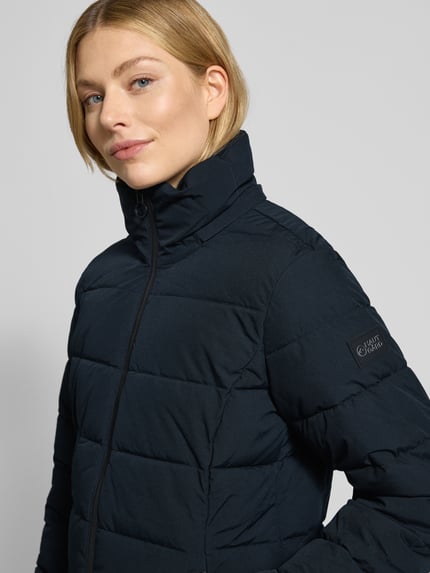 Frauenmodel trägt Steppmantel mit Sorona® Aura Filling von NAUTGÅRD in Schwarz, wasserabweisend, atmungsaktiv, Nahaufnahme Oberkörper.