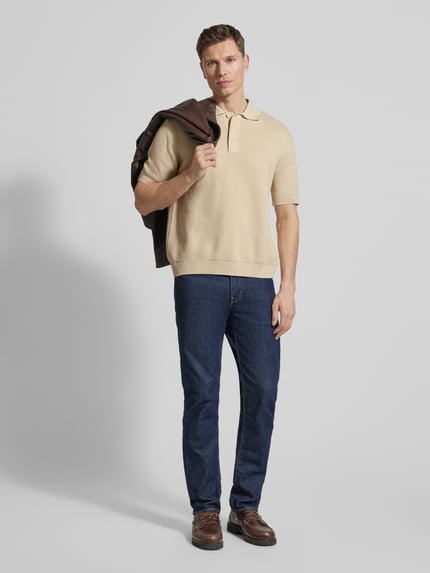 Männermodel trägt Relaxed Fit Poloshirt aus reiner Baumwolle Modell 'DANE' von SELECTED HOMME, beige, unifarben, Strickoptik, Ganzkörperansicht von vorne.