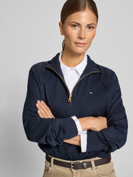 Frauenmodel trägt Pullover mit Troyerkragen von T. HILFIGER SPW., dunkelblau, gestreifte Strickstruktur, Logo-Detail, Nahaufnahme Oberkörper.