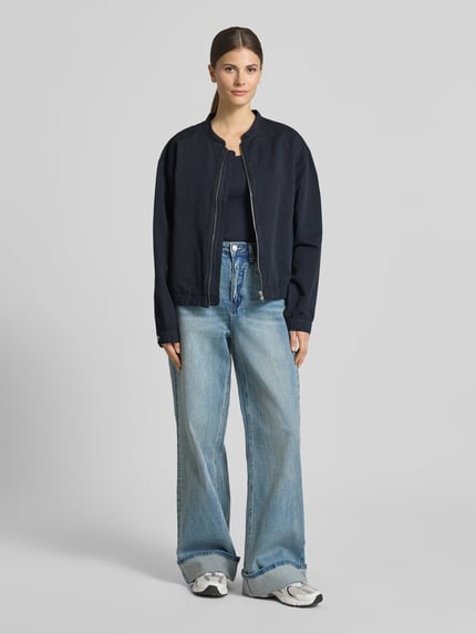 Kobiece model nosi kurtkę Jacke aus Baumwoll-Leinen-Mix mit Reißverschluss von Lanius, krój regular fit, stójka, mieszanka bawełny i lnu, zamek błyskawiczny, długość tyłu w rozmiarze 36: 58 cm, szerokość ramion w rozmiarze 36: 43 cm, szerokość klatki piersiowej w rozmiarze 36: 56 cm, długość rękawów w rozmiarze 36: 62 cm, ciemny kolor, gładka faktura, prosty krój; widok całej sylwetki z przodu.