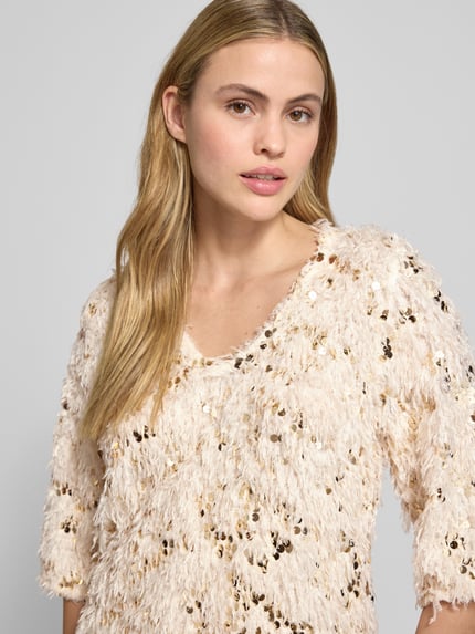 Frauenmodel trägt T-Shirt mit Federn und Pailletten Modell 'NOLLA' von FREE/QUENT in Creme, V-Ausschnitt, Paillettenakzente, Nahaufnahme Oberkörper.