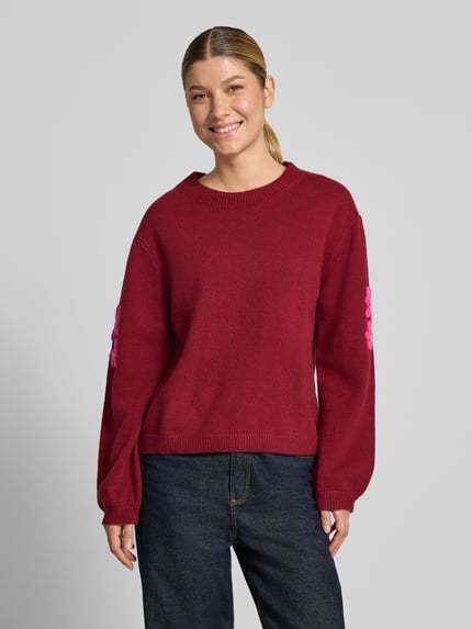 Frauenmodel trägt Strickpullover aus Wolle mit Stitchings und Perlen von Christian Berg Woman in Dunkelrot, Relaxed Fit, Jeans kombiniert, Ganzkörperansicht von vorne.