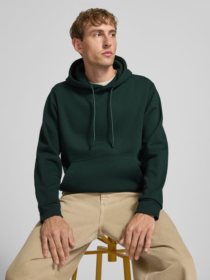 Männermodel trägt Hoodie mit Känguru-Tasche Modell 'BRADLEY' von JACK & JONES in Dunkelgrün, lockerer Schnitt, Nahaufnahme Oberkörper.