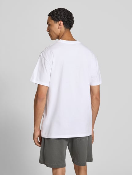 Männermodel trägt T-Shirt mit Logo-Stitching Modell 'Gracious' von Carhartt Work In Progress, weiß, Baumwolle, Ganzkörperansicht Rückansicht.