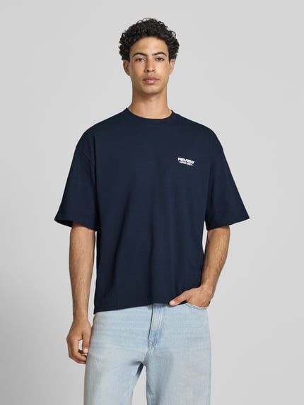 Męski model nosi T-Shirt mit Rundhalsausschnitt und Logo-Print od REVIEW, czysty bawełniany materiał, krój modern fit, kolor ciemnogranatowy, długość tyłu w rozmiarze M: 68 cm, widok całej sylwetki z przodu.