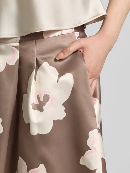 Vrouwenmodel draagt Midi-Rock aus Satin van s.Oliver BLACK LABEL met all-over motief, uitlopend, midilengte, bandplooien, zij-steekzakken, satijn materiaalverwerking, naadritssluiting, detailopname heup.