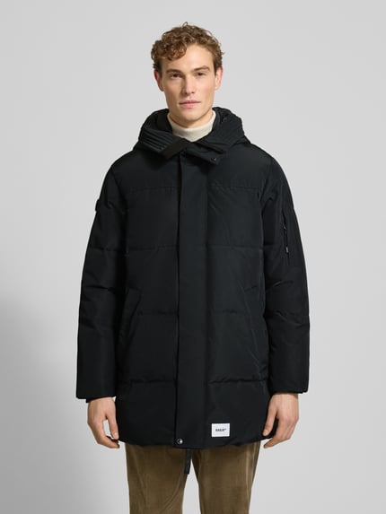 Männermodel trägt schwarzen Regular Fit Steppmantel mit Logo-Patch Modell 'Zeno' von khujo, Stepp-Optik, Ganzkörperansicht von vorne.
