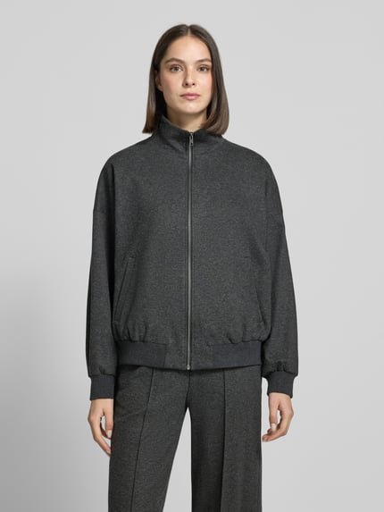 Frauenmodel trägt Jacke aus Viskose-Mix Modell 'EYAM' von DRYKORN in Dunkelgrau, Stehkragen, Reißverschluss, Eingrifftaschen, Ganzkörperansicht von vorne.