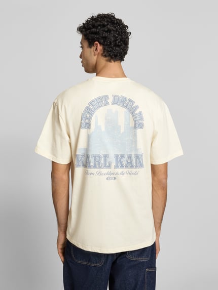 Männermodel trägt Oversized T-Shirt mit rückseitigem Print von KARL KANI aus reiner Baumwolle mit Label-Stitching, Ganzkörperansicht Rückansicht.