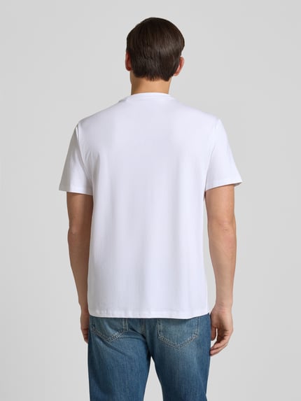Männermodel trägt T-Shirt mit Logo und Rundhalsausschnitt von Guess in Weiß, Baumwoll-Mix mit Modal, Relaxed Fit, Ganzkörperansicht Rückansicht.