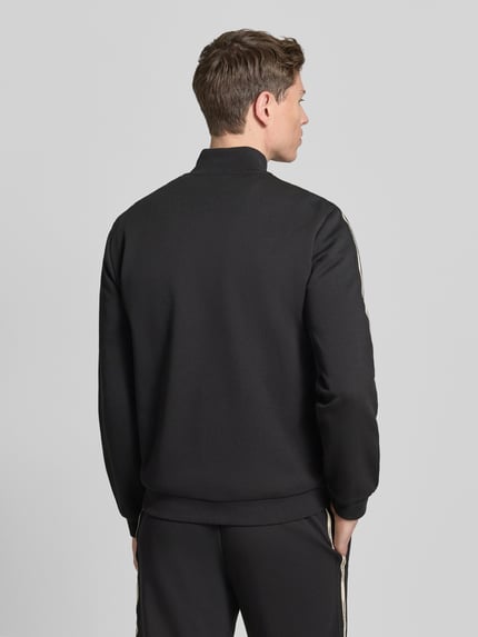 Männermodel trägt Sweatjacke mit Stehkragen und Zweiwege-Reißverschluss von EA7 Emporio Armani in Schwarz, Rückenansicht, Ganzkörperansicht Rückansicht. Regular Fit, Eingrifftaschen, Label-Detail, Rückenlänge 68 cm, Ärmellänge 67 cm.