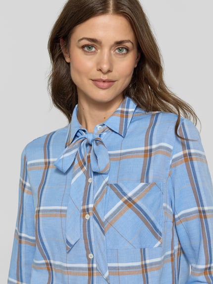 Frauenmodel trägt Regular Fit Schluppenbluse mit Brusttasche von MORE & MORE, kariertes Muster in Blau, Braun und Weiß, Nahaufnahme Oberkörper.