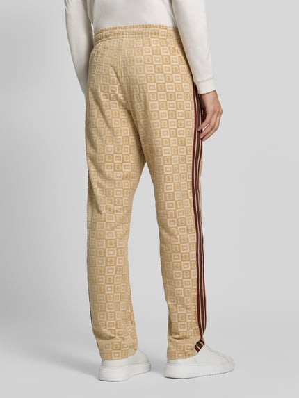 Männermodel trägt Straight Fit Sweatpants mit Label-Stitching von COLUCCI aus Baumwoll-Mix in Beige mit Muster, elastischer Bund, Ganzkörperansicht Rückansicht.