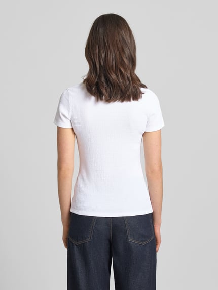 Frauenmodel trägt T-Shirt mit Label-Detail von Marc Cain, Weiß, kurzer Ärmel, elastisches Material, körpernah, Ganzkörperansicht Rückansicht.